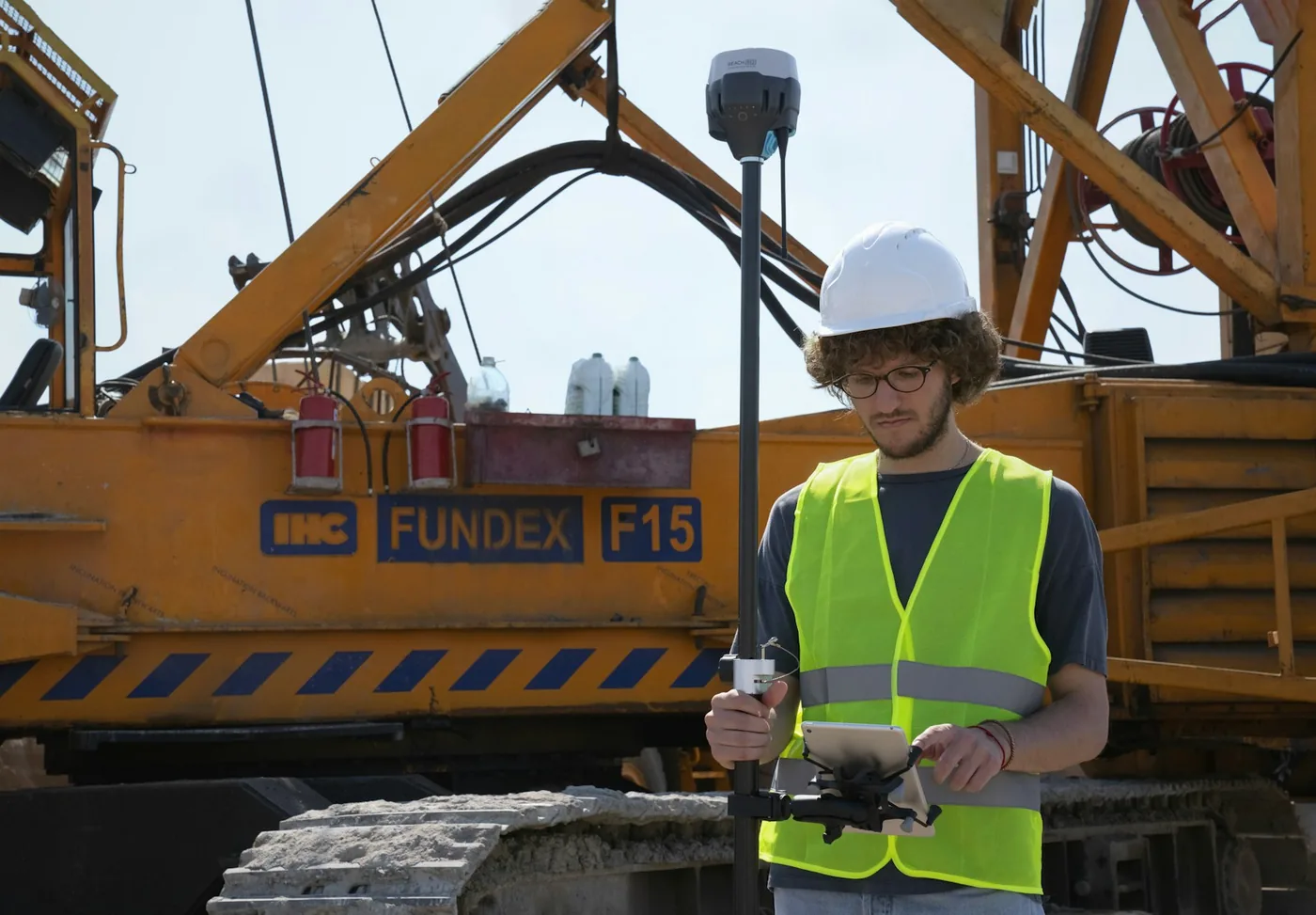 Surveyor in a hard hat and safety vest holding a survey pole on a construction site